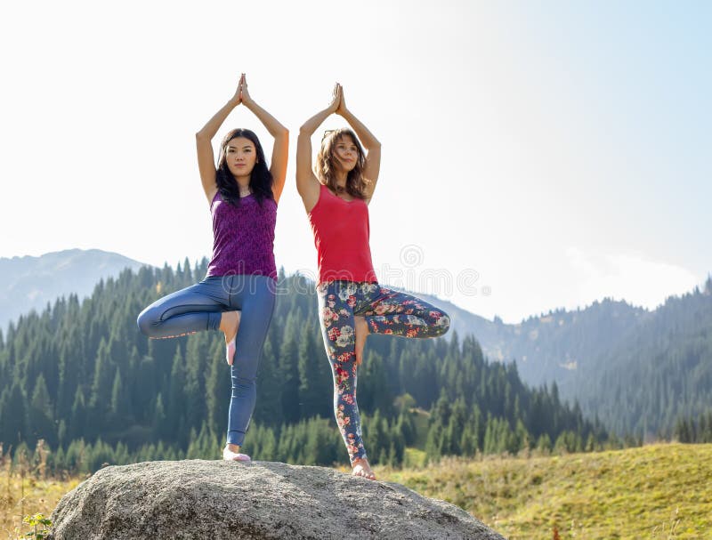 Dos mujeres jovenes que hacen yoga en una roca foto de archivo Dos mujeres jovenes que hacen yoga en una roca foto de archivo