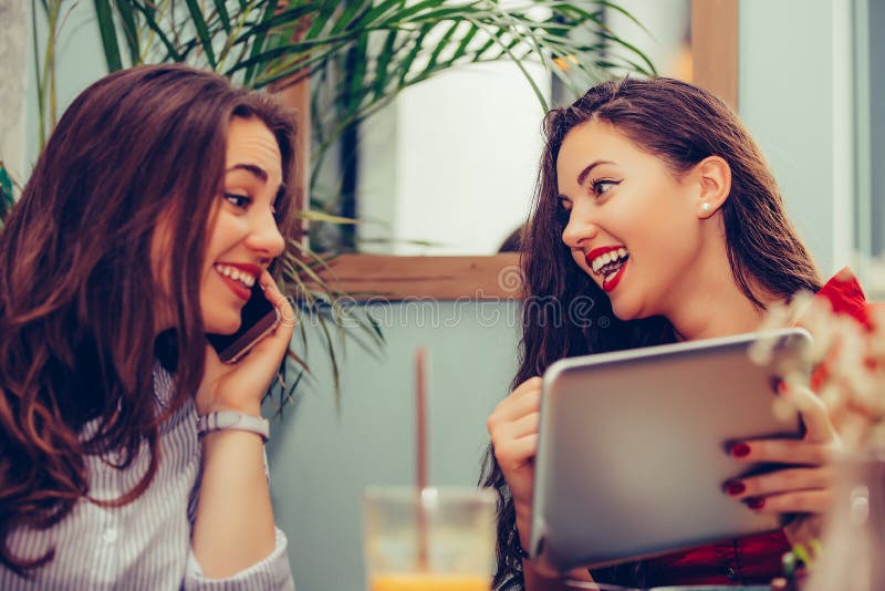 Dos mujeres jovenes que se sientan en café, hablando y mirando algo en la tableta digital imagen de archivo libre de regalías Dos mujeres jovenes que se sientan en café, hablando y mirando algo en la tableta digital imagen de archivo libre de regalías