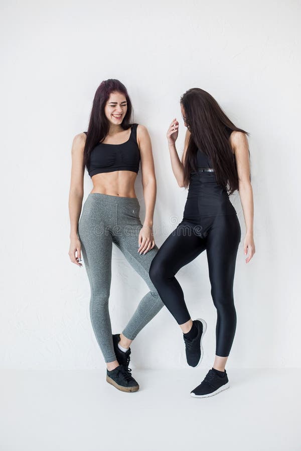 Dos mujeres juguetonas hermosas felices en deporte se adaptan a sonrisa mientras que presentan en el fondo blanco Retrato integra foto de archivo Dos mujeres juguetonas hermosas felices en deporte se adaptan a sonrisa mientras que presentan en el fondo blanco Retrato integra foto de archivo