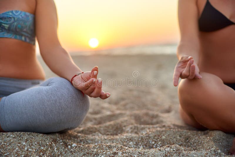 Dos mujeres que hacen la meditación del grupo en la playa en salida del sol Amigos femeninos que hacen el padmasana de la yoga o fotos de archivo Dos mujeres que hacen la meditación del grupo en la playa en salida del sol Amigos femeninos que hacen el padmasana de la yoga o fotos de archivo
