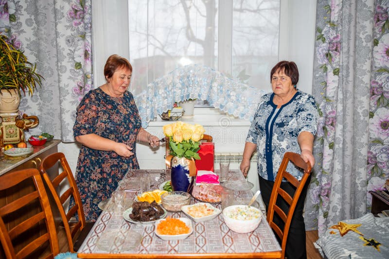 Dos mujeres rusas de 70 y 60 años preparan una mesa festiva con platos tradicionales fotos de archivo libres de regalías