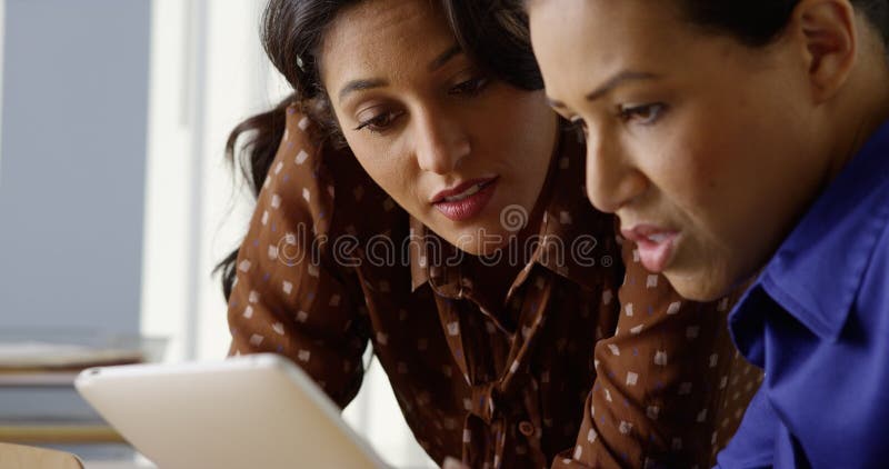 Dos negros y mujeres de negocios hispánicas que trabajan en la tableta foto de archivo Dos negros y mujeres de negocios hispánicas que trabajan en la tableta foto de archivo