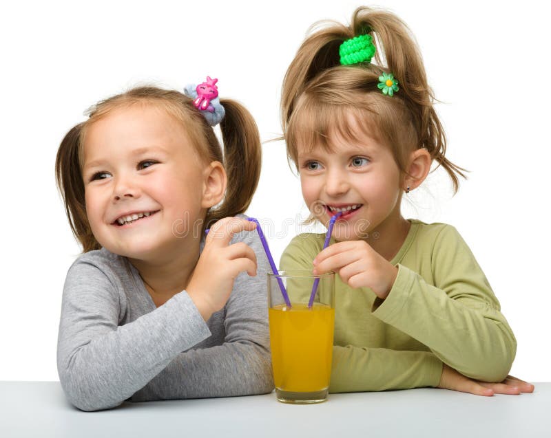 Dos niñas están bebiendo el zumo de naranja fotografía de archivo Dos niñas están bebiendo el zumo de naranja fotografía de archivo