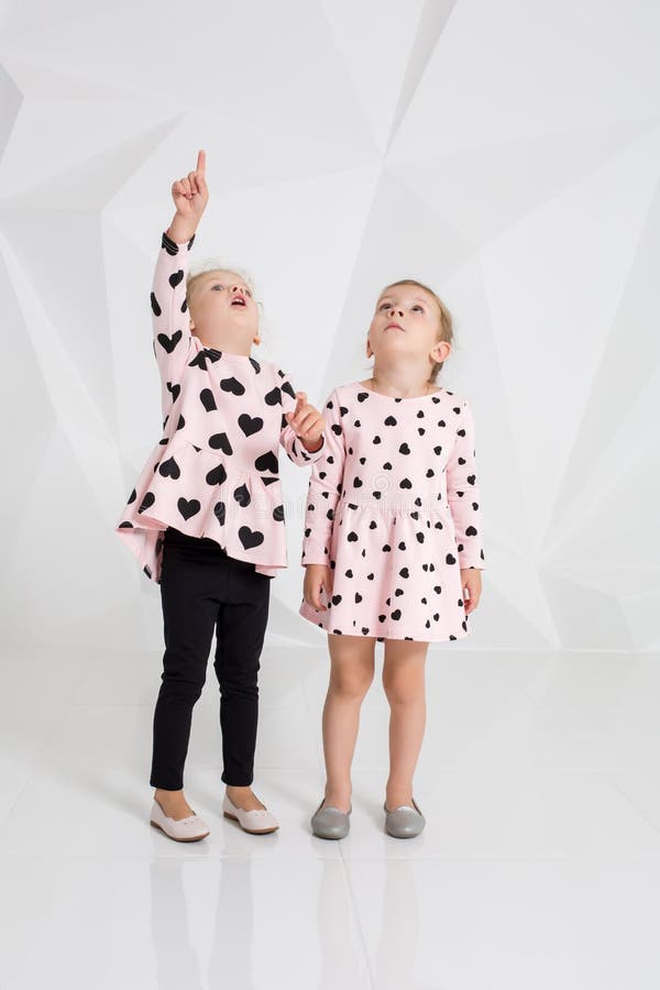 Dos niñas lindas que se colocan en ropa rosada con los corazones negros en el fondo blanco de la pared en el estudio imagen de archivo libre de regalías Dos niñas lindas que se colocan en ropa rosada con los corazones negros en el fondo blanco de la pared en el estudio imagen de archivo libre de regalías