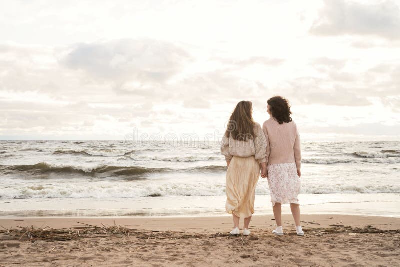 Dos niñas van de la mano al mar. caminar por el océano en otoño con ropa de abrigo. relaciones entre mujeres. foto de archivo libre de regalías
