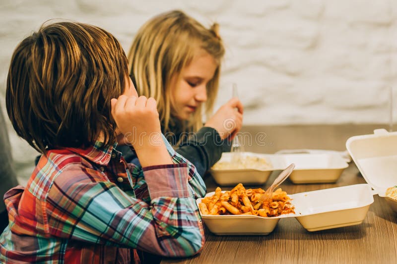 Dos niños lindos comen las pastas de los espaguetis en restaurante de los alimentos de preparación rápida