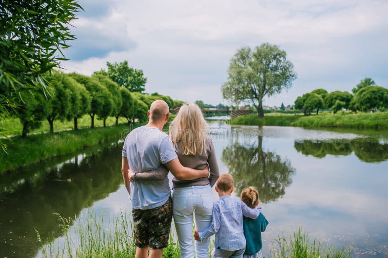 Dos niños, madre y padre mirando en el lago en la opinión trasera del día de verano imagenes de archivo Dos niños, madre y padre mirando en el lago en la opinión trasera del día de verano imagenes de archivo