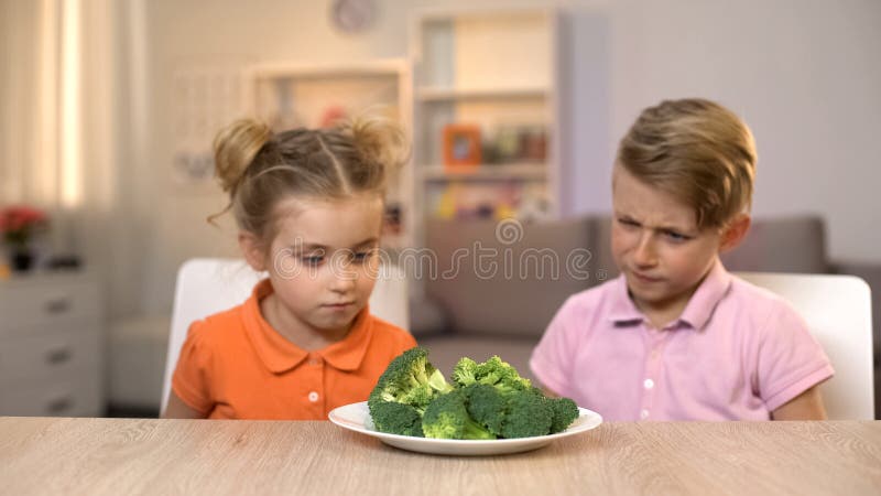 Dos niños que miran el bróculi, comida poco apetitosa, comida sana insípida imagen de archivo libre de regalías Dos niños que miran el bróculi, comida poco apetitosa, comida sana insípida imagen de archivo libre de regalías