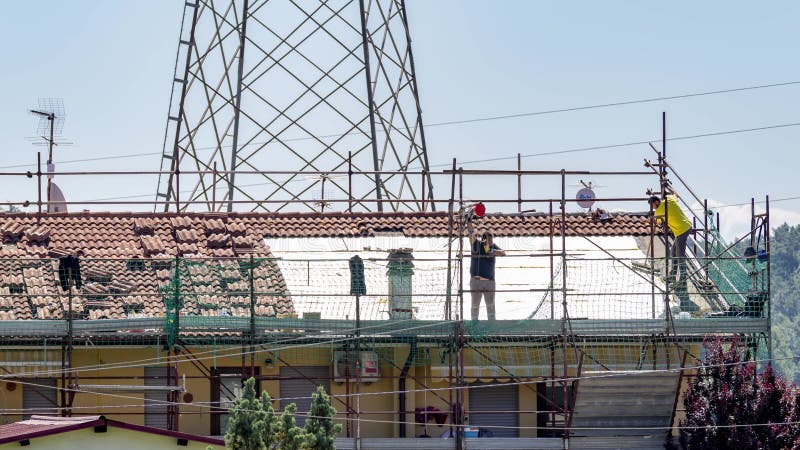 Dos obreros de la construcción en el tejado de un edificio de departamentos lo enlosaron en italia toscana