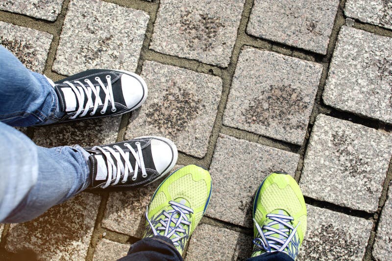 Two pairs of running shoe and slipper shoe standing together on grey brick walkway, tourist couple traveling. Two pairs of running shoe and slipper shoe standing together on grey brick walkway, tourist couple traveling