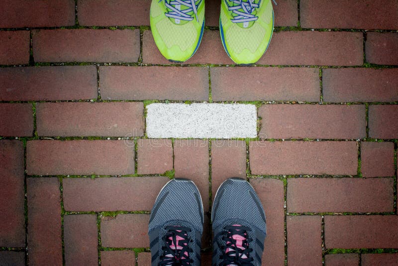 Two pairs of running shoes standing behind each others on red brick walkway with white line separate , Runner couple exercising. Two pairs of running shoes standing behind each others on red brick walkway with white line separate , Runner couple exercising