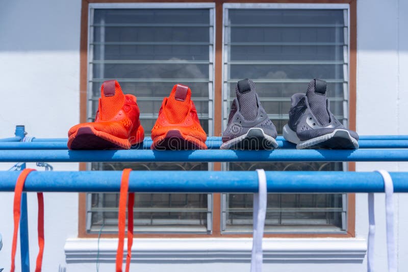Two pairs of running shoes, red and grey, putted on the cloths hanger to dry in the sun after washing inside the back of the house. Two pairs of running shoes, red and grey, putted on the cloths hanger to dry in the sun after washing inside the back of the house.