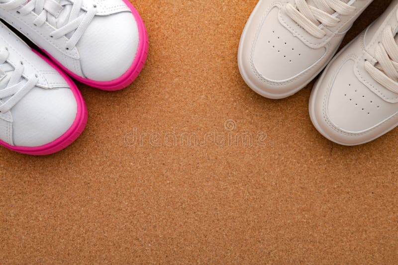 two pairs of children's sneakers for boy and girl on cork floor. View from above. Space for text. two pairs of children's sneakers for boy and girl on cork floor. View from above. Space for text.