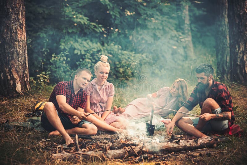 Dos pares que tienen comida campestre en bosque Hombre barbudo y su mejor amigo que cocinan las salchichas sobre el fuego Caminan foto de archivo libre de regalías Dos pares que tienen comida campestre en bosque Hombre barbudo y su mejor amigo que cocinan las salchichas sobre el fuego Caminan foto de archivo libre de regalías