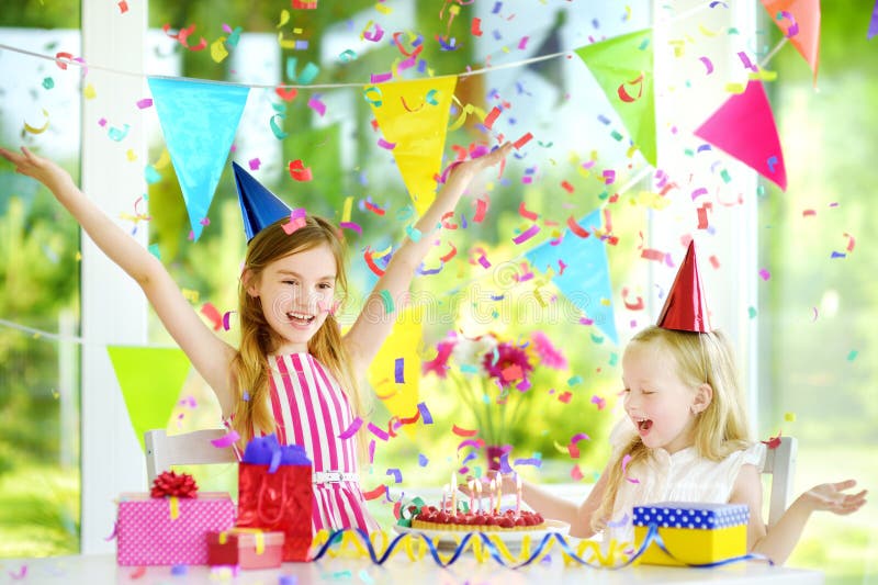 Dos pequeñas hermanas divertidas que tienen fiesta de cumpleaños en casa, soplando velas en la torta de cumpleaños imagen de archivo libre de regalías Dos pequeñas hermanas divertidas que tienen fiesta de cumpleaños en casa, soplando velas en la torta de cumpleaños imagen de archivo libre de regalías
