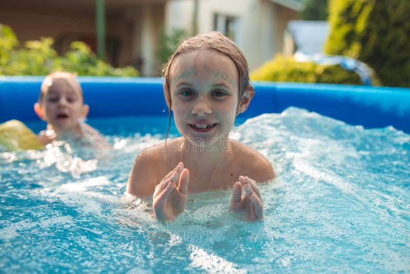 Dos pequeñas hermanas lindas alegres que juegan y que se divierten, salpicando y saltando en piscina inflable en el patio trasero imagen de archivo libre de regalías Dos pequeñas hermanas lindas alegres que juegan y que se divierten, salpicando y saltando en piscina inflable en el patio trasero imagen de archivo libre de regalías