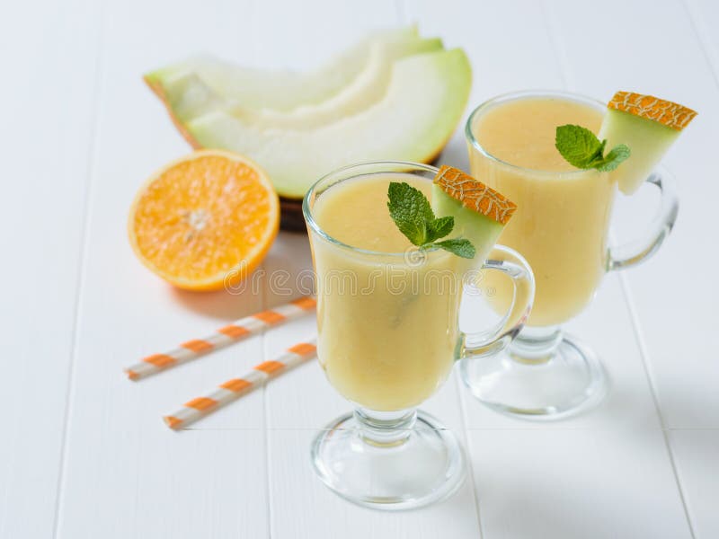 Dos tazas de cristal con los pedazos de melón y de menta en una tabla de madera blanca fotografía de archivo Dos tazas de cristal con los pedazos de melón y de menta en una tabla de madera blanca fotografía de archivo