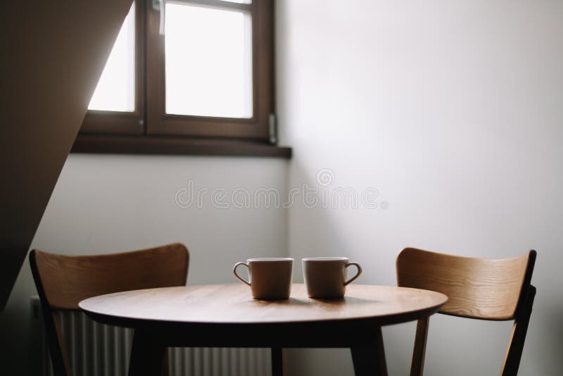 Dos tazas en la tabla de madera Comedor con la tabla y dos sillas Interior nórdico escandinavo mínimo moderno Caf? de la ma?ana imagenes de archivo Dos tazas en la tabla de madera Comedor con la tabla y dos sillas Interior nórdico escandinavo mínimo moderno Caf? de la ma?ana imagenes de archivo