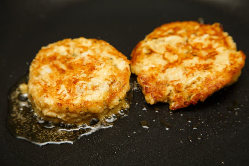 Two crab cakes frying in a saute pan in hot oil. Two crab cakes frying in a saute pan in hot oil