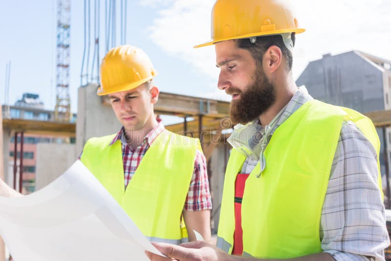 Dos trabajadores de construcción jovenes que analizan junto el plan de a imagen de archivo libre de regalías Dos trabajadores de construcción jovenes que analizan junto el plan de a imagen de archivo libre de regalías