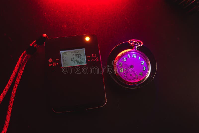 Dosimètre de rayonnement radioactif à côté d'une vieille montre de poche avec une peinture fluorescente dangereuse. lumière violet photo libre de droits