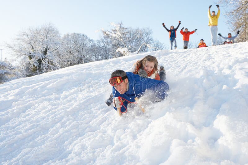 Father And Daughter Having Fun Sledging Down Hill with family watching. Father And Daughter Having Fun Sledging Down Hill with family watching