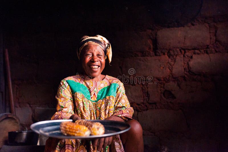 Douala Cameroon - 06 august 2018: closeup of old african lady in her rural home kitchen with traditional dress looking in camera. Smiling african lady offering royalty free stock image Douala Cameroon - 06 august 2018: closeup of old african lady in her rural home kitchen with traditional dress looking in camera. Smiling african lady offering royalty free stock image