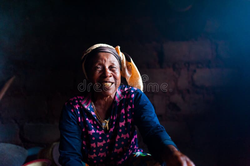 Douala Cameroon - 06 august 2018: closeup of old african lady in her rural home kitchen with traditional dress looking straight in. Old african lady inside home stock photos Douala Cameroon - 06 august 2018: closeup of old african lady in her rural home kitchen with traditional dress looking straight in. Old african lady inside home stock photos