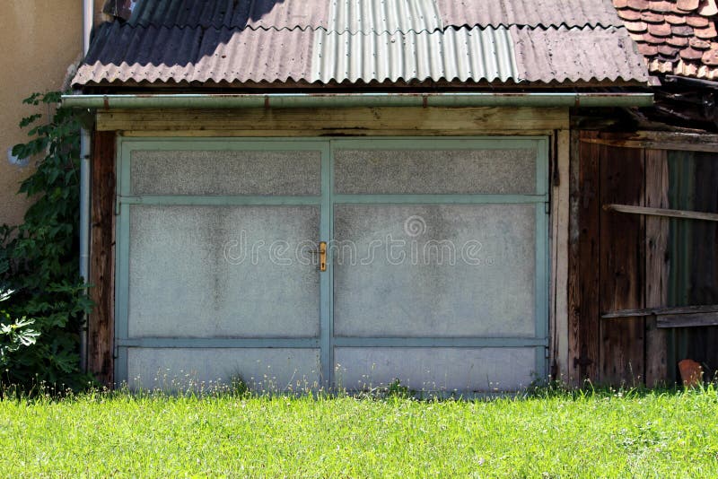Double elongated large old vintage retro garage doors with blue metal frame and dirty grey panels mounted on wooden garage. Double elongated large old vintage stock photo Double elongated large old vintage retro garage doors with blue metal frame and dirty grey panels mounted on wooden garage. Double elongated large old vintage stock photo