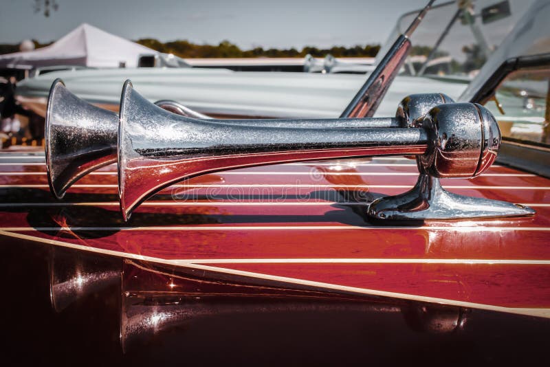 Double horns on vintage wooden speedboat with reflections in wood and other boats and marina in background