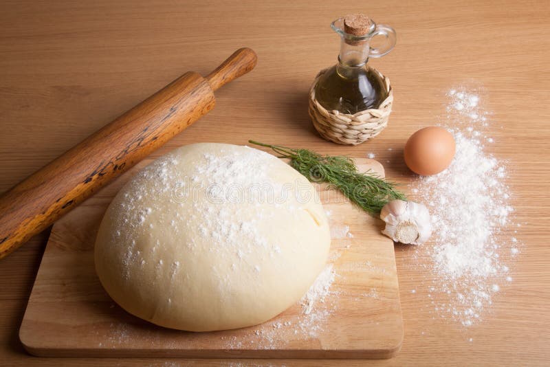 dough on a board with flour. olive oil, eggs, rolling pin, garlic and dill for stuffing
