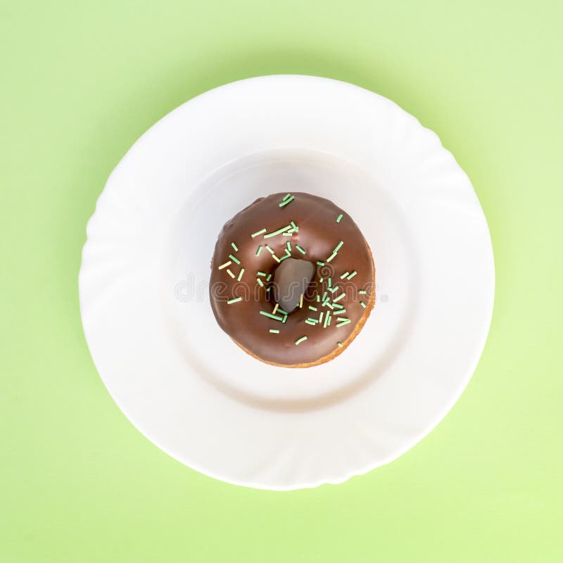 Doughnut met chocoladeglans wordt en met groene buizen op witte plaat wordt bestrooid behandeld die die