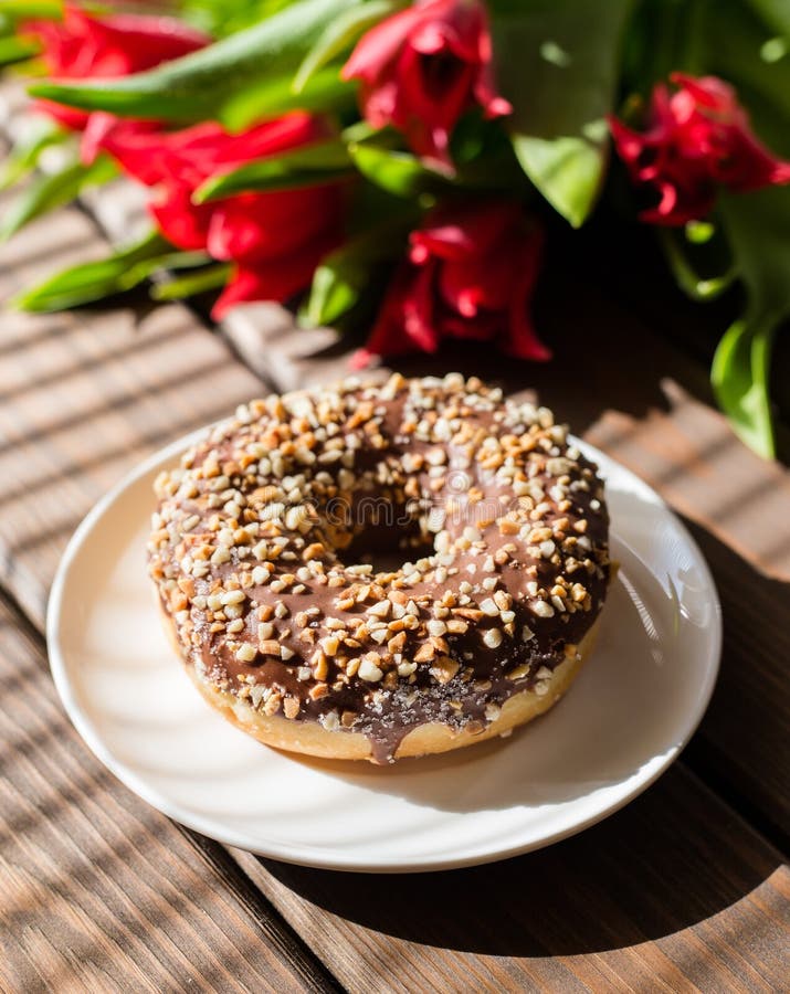 Doughnut στο άσπρο πιάτο με τις τουλίπες σε ένα καφετί ξύλινο υπόβαθρο Πρόγευμα στο θερινό χρόνο στοκ εικόνα Doughnut στο άσπρο πιάτο με τις τουλίπες σε ένα καφετί ξύλινο υπόβαθρο Πρόγευμα στο θερινό χρόνο στοκ εικόνα