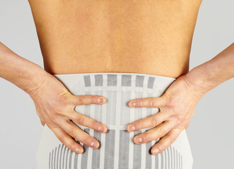 Concept image of a woman holding her hands on her back wearing a lumbal bandage to emphasize an issue with inflammation and lower back pain. Image on white background, taken from behind. Concept image of a woman holding her hands on her back wearing a lumbal bandage to emphasize an issue with inflammation and lower back pain. Image on white background, taken from behind.