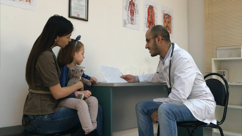 Doutor de sorriso que explica o cardiograma à mãe e à menina foto de stock Doutor de sorriso que explica o cardiograma à mãe e à menina foto de stock