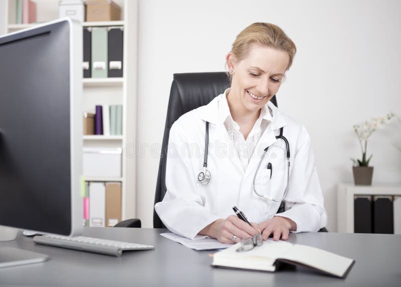 Doutor feliz Making Medical Reports da mulher na tabela foto de stock Doutor feliz Making Medical Reports da mulher na tabela foto de stock