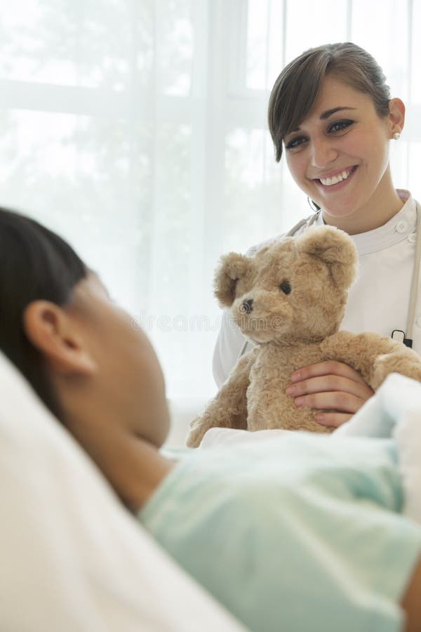 Smiling female doctor giving a teddy bear to a girl patient lying down on a hospital bed. Smiling female doctor giving a teddy bear to a girl patient lying down on a hospital bed