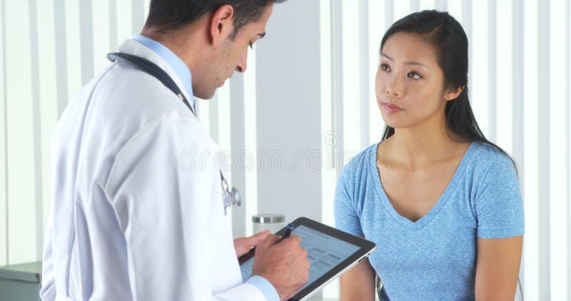 Doutor latino-americano que faz perguntas pacientes asiáticas imagem de stock Doutor latino-americano que faz perguntas pacientes asiáticas imagem de stock