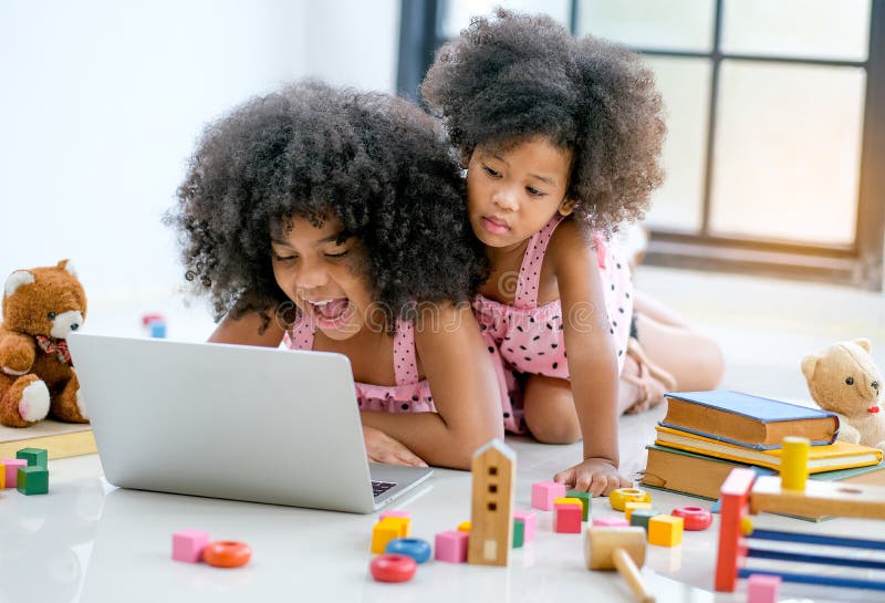 Două tinere africane se joacă cu un notebook printre jucării și cărți în fața ferestrei de sticlă stock image