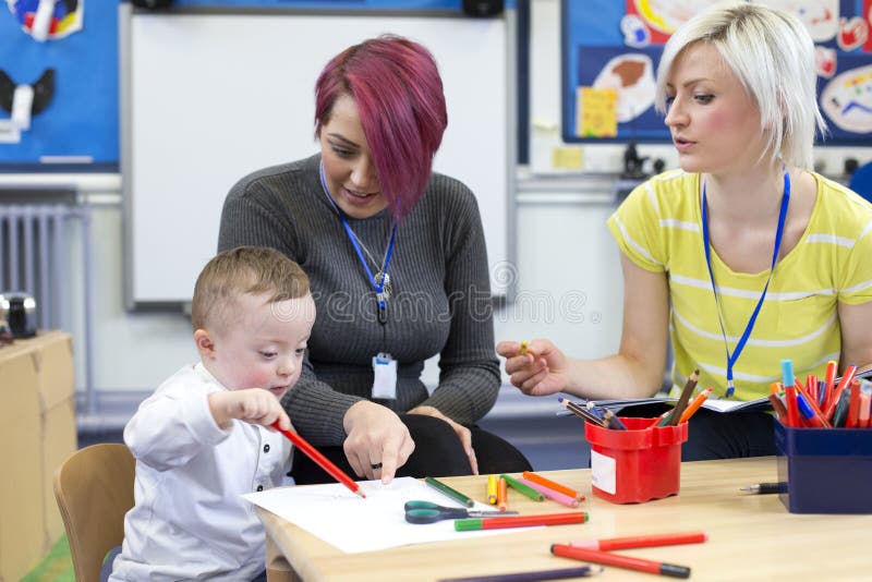Down Syndrome boy at Nursery. Nursery teacher sitting with a parent and her Down Syndrome son in the classroom. they are discussing the little boys progress royalty free stock image Down Syndrome boy at Nursery. Nursery teacher sitting with a parent and her Down Syndrome son in the classroom. they are discussing the little boys progress royalty free stock image