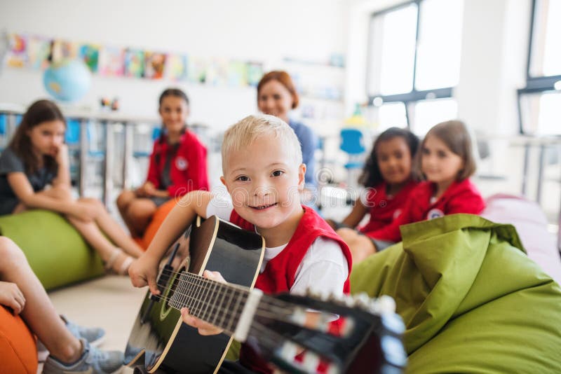 A down-syndrome boy with school kids and teacher sitting in class, playing guitar. A down-syndrome boy with school kids and teacher sitting on the floor in stock images A down-syndrome boy with school kids and teacher sitting in class, playing guitar. A down-syndrome boy with school kids and teacher sitting on the floor in stock images
