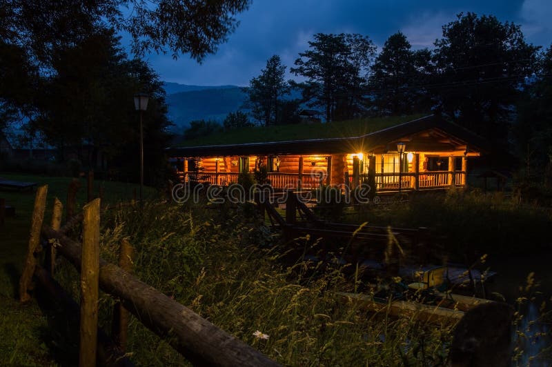 Downshifting lifestyle. Summer night. Wooden cabin hut in the Carpathian Mountains, illuminated by the warm light of lanterns