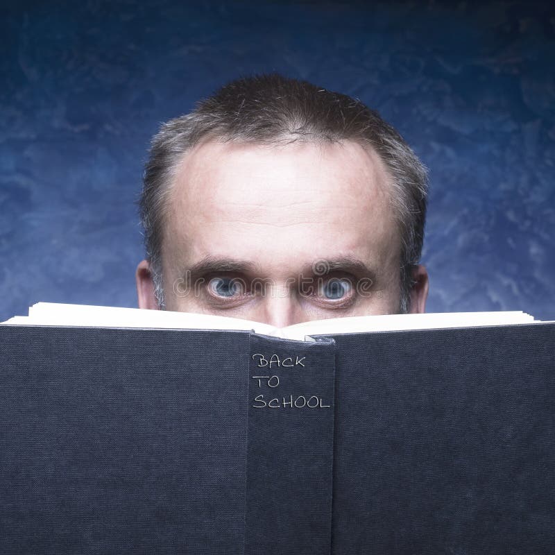 Dra tillbaka till skolan som är skriftlig på den svarta boken Mogen man bak boken på blå bakgrund royaltyfria foton Dra tillbaka till skolan som är skriftlig på den svarta boken Mogen man bak boken på blå bakgrund royaltyfria foton