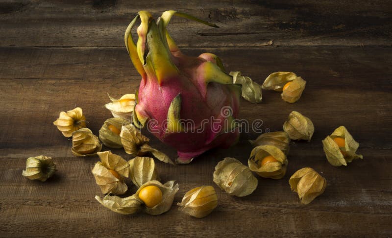 Whole Dragon fruit on wooden plank surrounded by gooseberries. Whole Dragon fruit on wooden plank surrounded by gooseberries