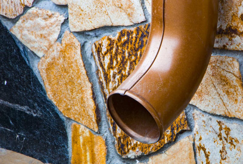 A Drain Pipe Attached To a Wall of Multicolored Stone Stock Photo