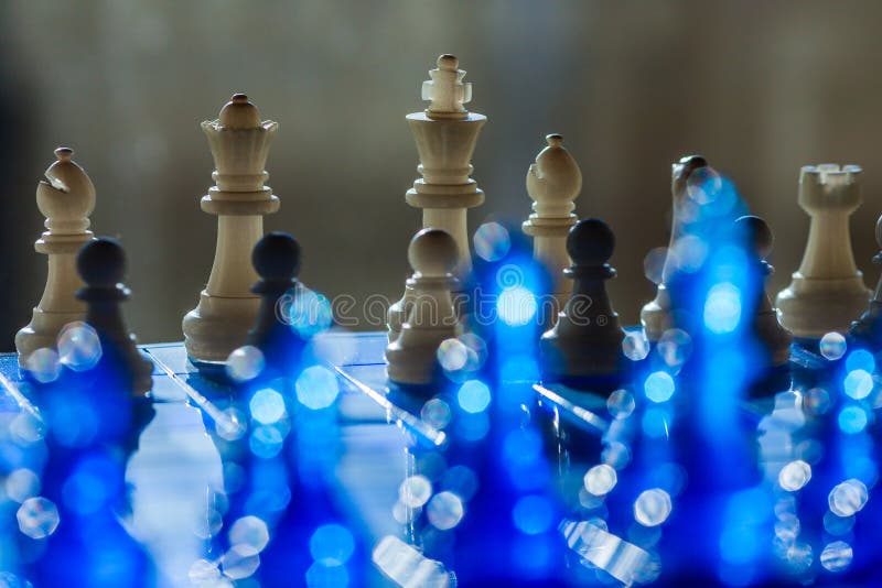 A dramatic chess scene features wooden pieces on a reflective blue surface stock photos