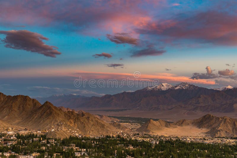 Dramatic colorful sunset with mountains cover with snow and small city below Dramatic overcast sky.