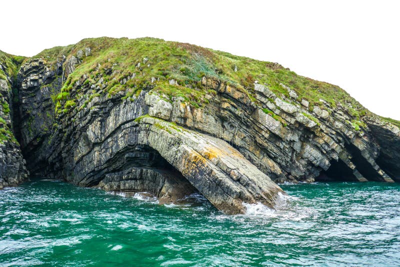 Dramatic curved rock layers plunge from clifftop into teal and aqua ocean waves on Loop Head Peninsula, County Clare, Ireland.