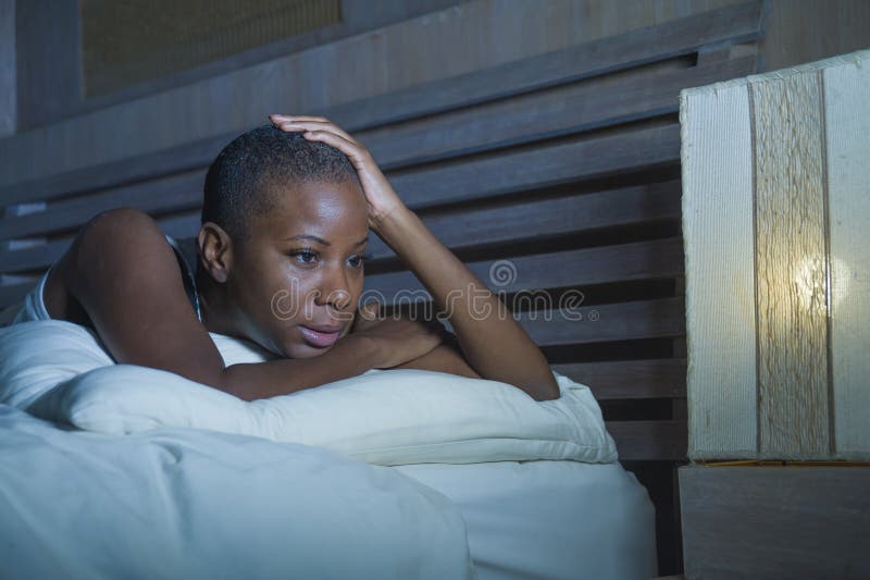 Dramatic lifestyle portrait of young sad and depressed black african American woman on bed sleepless suffering headache insomnia s