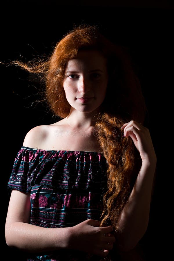 Dramatic portrait of sad red haired model with shadow on her face and freckles